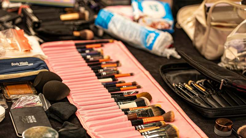 Two hands arranging cream eyeshadows in a custom-fit rosewood makeup drawer with labeled silicone dividers